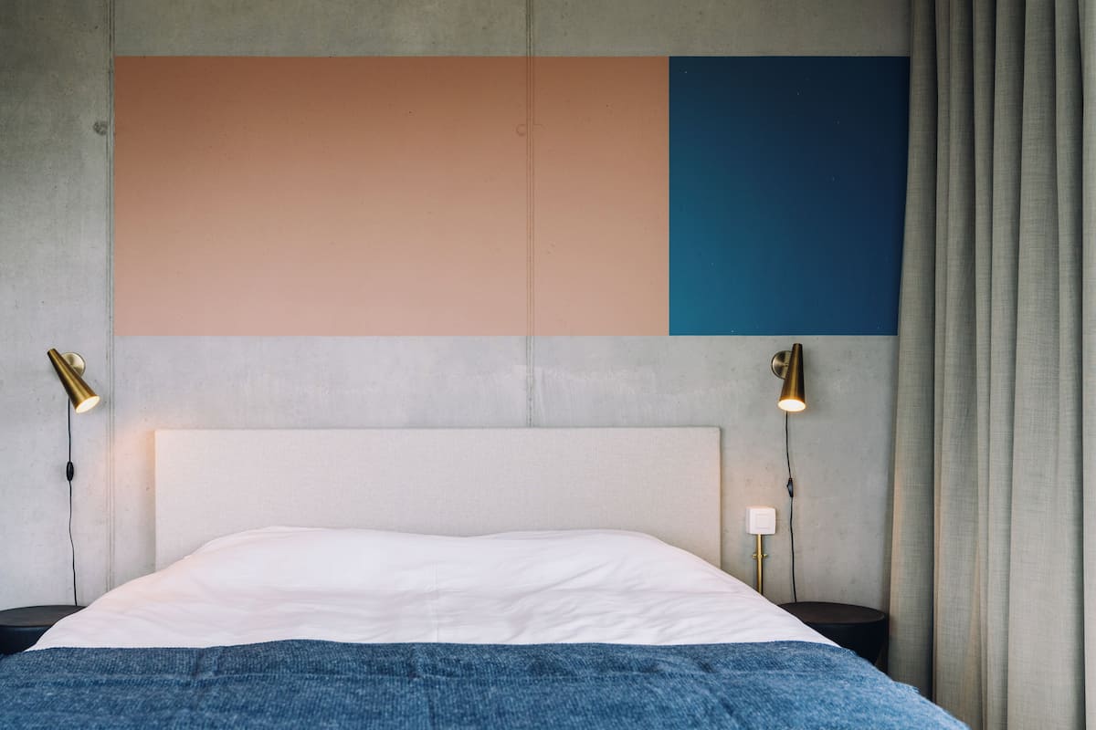 Ein Bett mit weißem Kopfteil, zwei Nachttischlampen und einer blauen Decke.