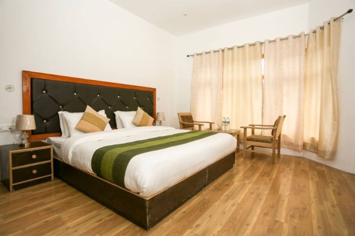 A hotel room with a large bed, a wooden headboard, a nightstand, a chair, and a window with curtains.