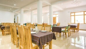 Un comedor espacioso con sillas y mesas de madera, techos altos con iluminación empotrada y ventanas amplias que dejan entrar luz natural.