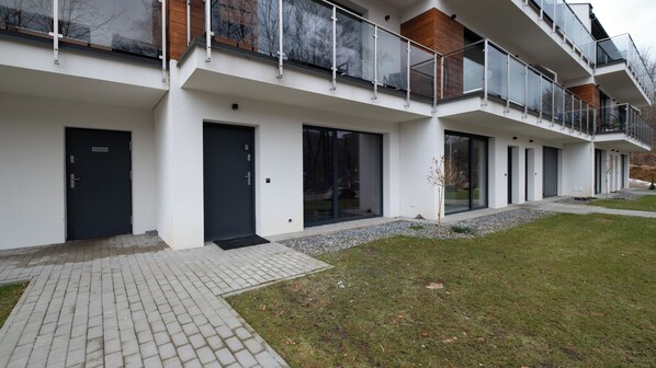 En modern byggnad med en slät fasad, stora fönster och en liten trädgårdsyta.