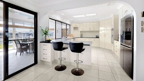 A modern kitchen with a central island, two bar stools, and a view of the outside through large windows. - Relfections at Newport 5Bedroom Pool and Canal Living (Newport)