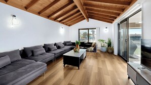 A modern living room with a wooden ceiling, grey sofas, a glass coffee table, and a TV on a wooden stand. - Relfections at Newport 5Bedroom Pool and Canal Living (Newport)