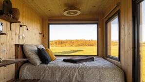 A cozy bedroom with a large window, wooden walls, a bed with patterned bedding, and a bench. - L'Échappée Royale - Tiny House 20 minutes from Beauval Zoo (Billy)