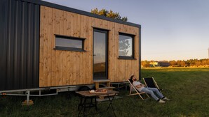 A modern wooden cabin with two windows and a door, a picnic table, and a person relaxing on a lawn chair. - L'Échappée Royale - Tiny House 20 minutes from Beauval Zoo (Billy)