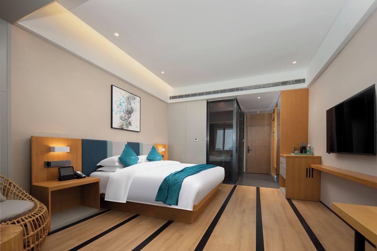 A modern hotel room with a large bed, bedside tables, a desk, a chair, a TV, and a sliding door leading to a bathroom.