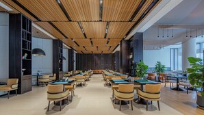 Une salle de conférence spacieuse, dotée de longues tables et de chaises, de panneaux de plafond en bois et de grandes fenêtres.