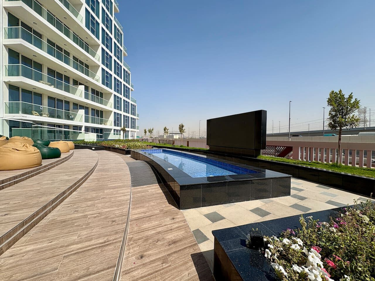 A modern outdoor pool area with a built-in seating area and a large flat-screen TV.