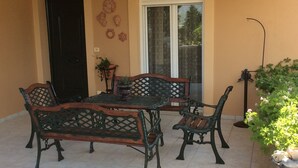 Een terras met een tafel, twee banken, een deur en een raam met uitzicht op groen.