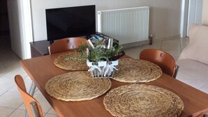 Een eethoek met een houten tafel, geweven placemats en een decoratie van groen en keukengerei.