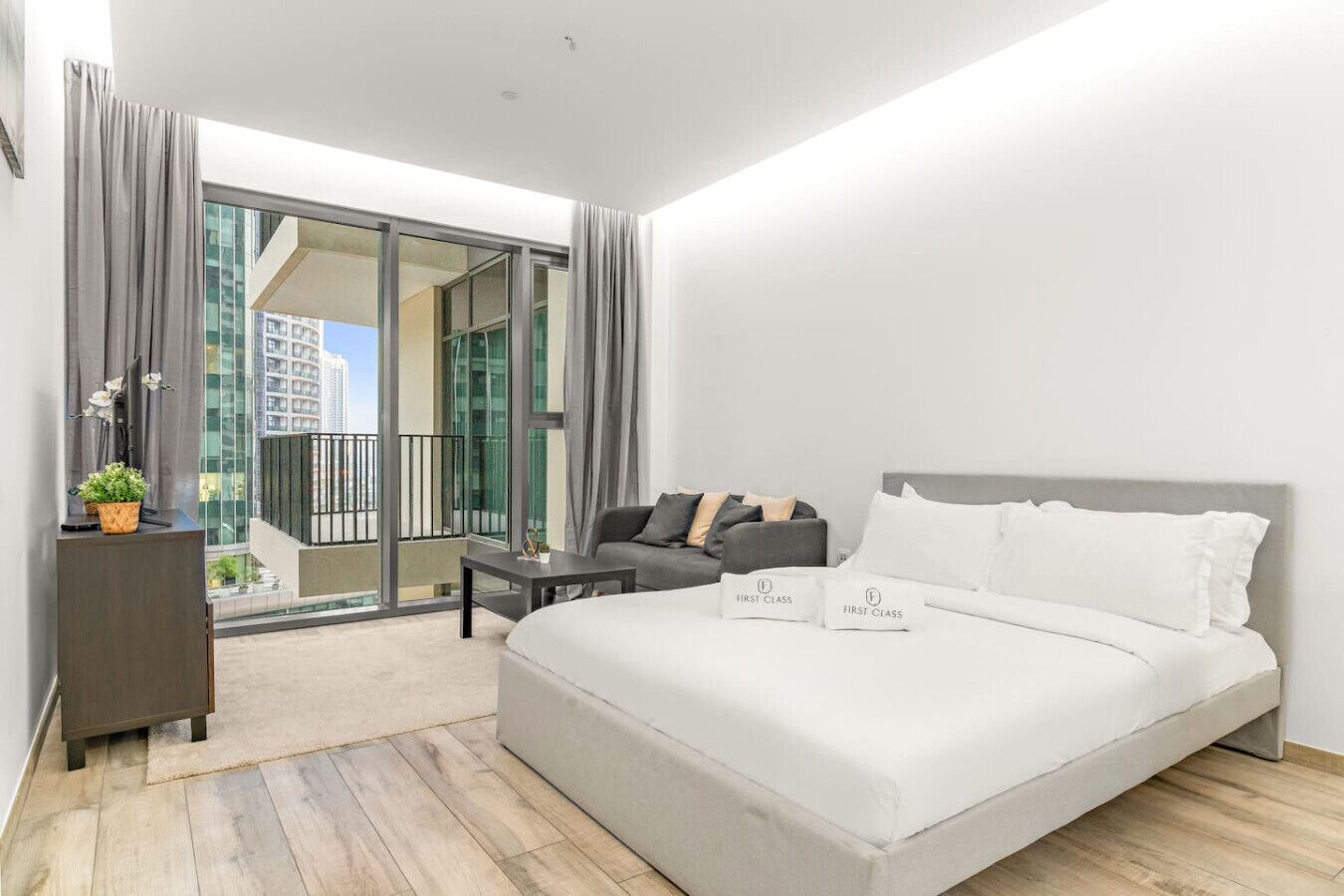Een moderne slaapkamer met een groot bed, een bank, een klein tafeltje en een stadsgezicht door grote ramen.