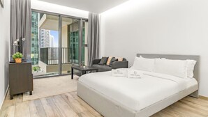 Een moderne slaapkamer met een groot bed, een bank, een klein tafeltje en een stadsgezicht door grote ramen.
