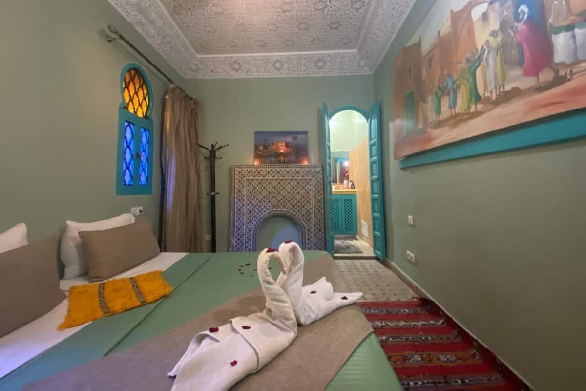 A room with a bed, a fireplace, a painting, and a door leading to another room.