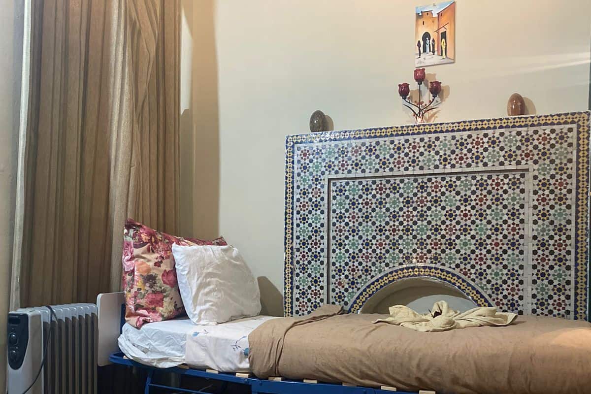 A bedroom with a bed, a radiator, a curtain, and a wall-mounted picture.
