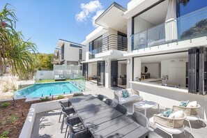 A modern two-story house with a swimming pool, outdoor seating, and a balcony.