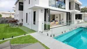 Una casa moderna de dos pisos con un balcón de vidrio que da a una piscina.