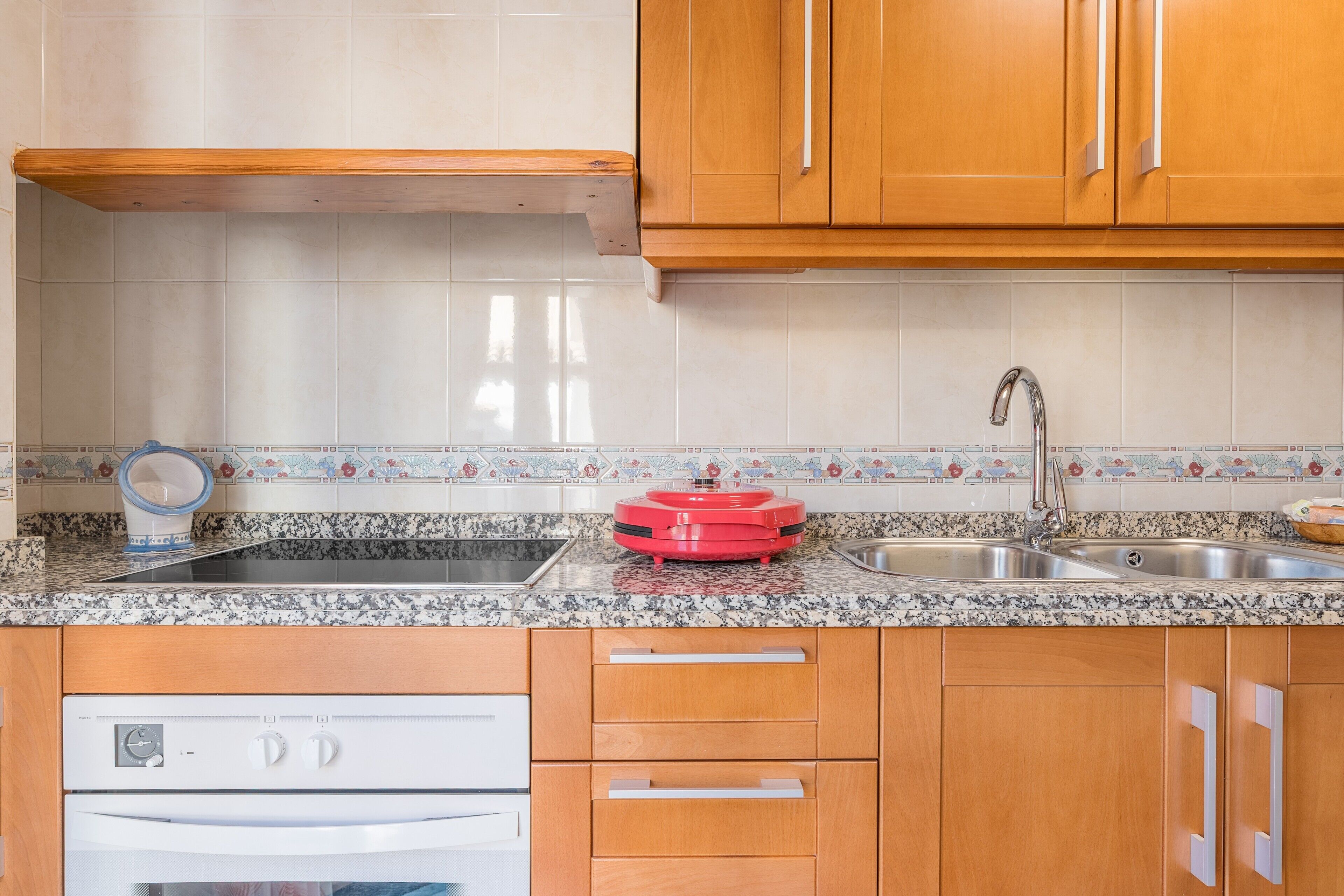 Una cocina con encimeras de granito, armarios de madera, horno empotrado y un electrodoméstico rojo sobre la encimera.