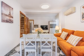 Una sala de estar con un sofá, una mesa de comedor con sillas, un televisor y una escalera que lleva a otra habitación.