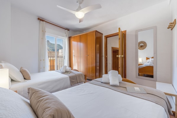 Habitación de hotel con dos camas, un armario, ventilador de techo, ventana con cortinas y un espejo.