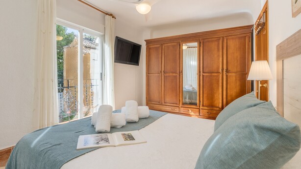 Ein Schlafzimmer mit einem Bett, einem Holzschrank, einem Deckenventilator und einem Fenster mit Vorhängen.
