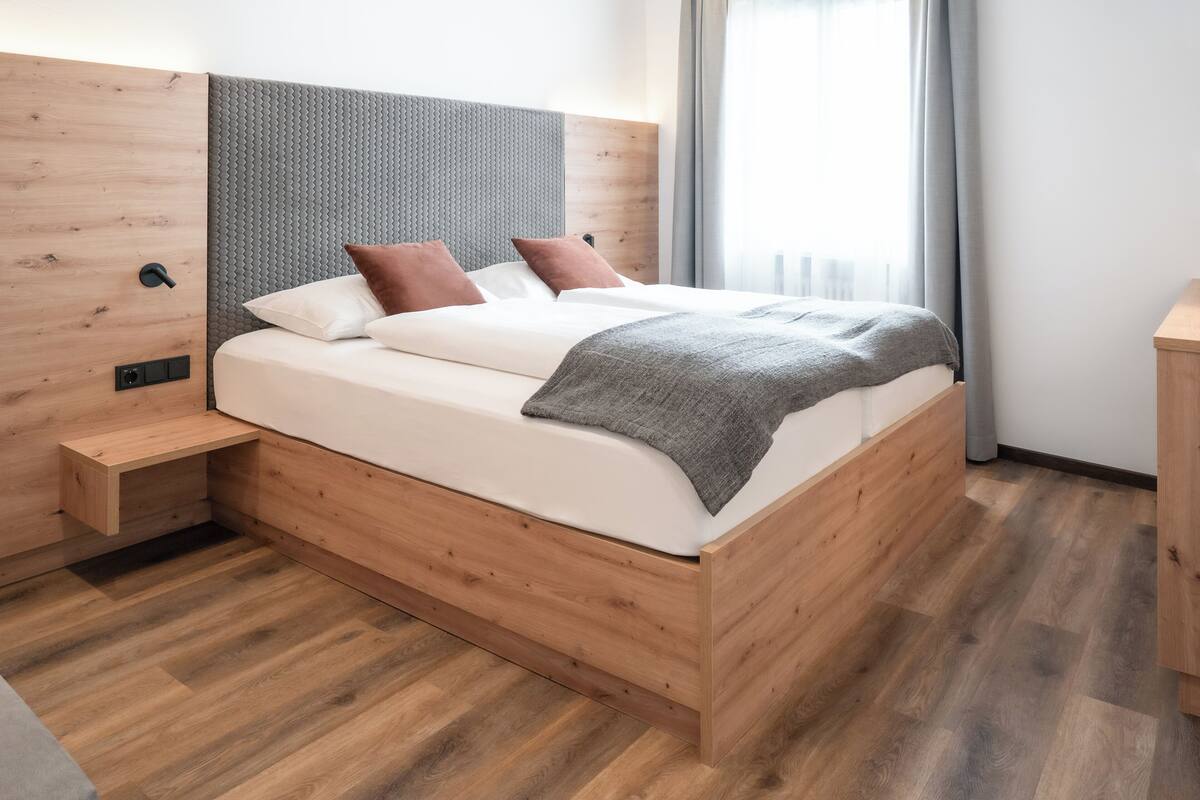 Une chambre à coucher moderne avec un cadre de lit en bois, une tête de lit grise texturée et un plaid gris.