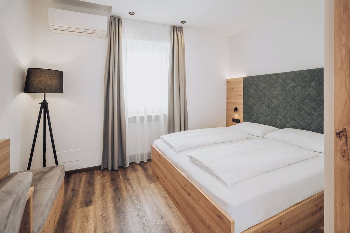 Une chambre d’hôtel avec un lit en bois, un bureau avec une lampe et une fenêtre avec des rideaux.