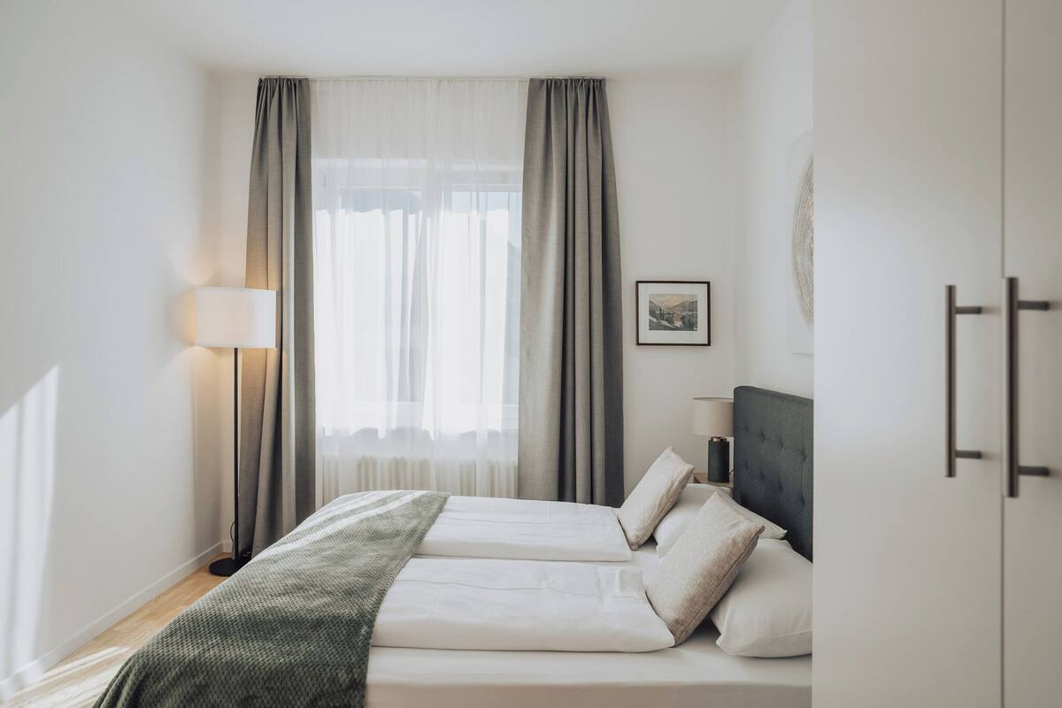 Une chambre avec deux lits, une table de chevet, une lampe et une fenêtre avec des rideaux.
