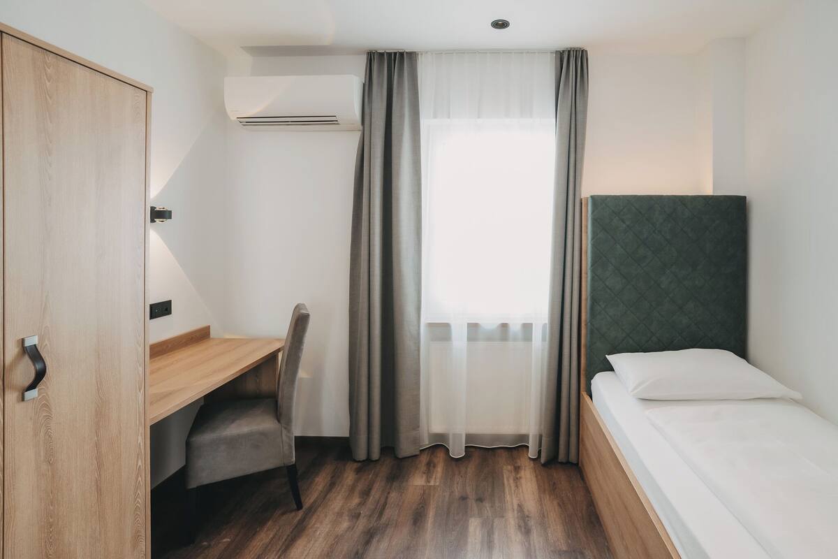Une chambre avec un lit, un bureau, une chaise, une armoire et une fenêtre avec des rideaux.