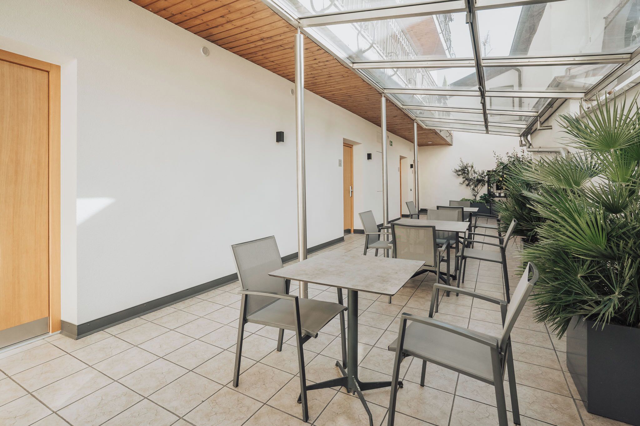 Un espacio interior moderno con techo de vidrio, piso de baldosas y varias mesas y sillas dispuestas para comer o celebrar reuniones.