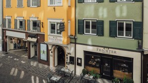 Ein Hotel mit gelber Fassade, grünen Fensterläden und Außenbestuhlung.
