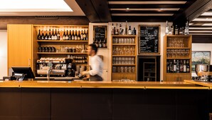 Eine Bar mit Regalen voller Flaschen und Gläsern, einer Kreidetafel mit Speisekarte und einer Kaffeemaschine.