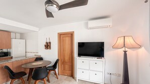 Un espacio habitable compacto con comedor, un televisor en un mueble, un ventilador de techo y una lámpara.