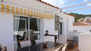 Un patio con una mesa y sillas de vidrio, un toldo a rayas amarillas y vistas de los edificios circundantes.
