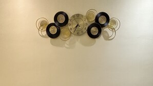 En grå sofa med to puder med mønster, et vægur og en dekorativ metalvæg med cirkulære detaljer.