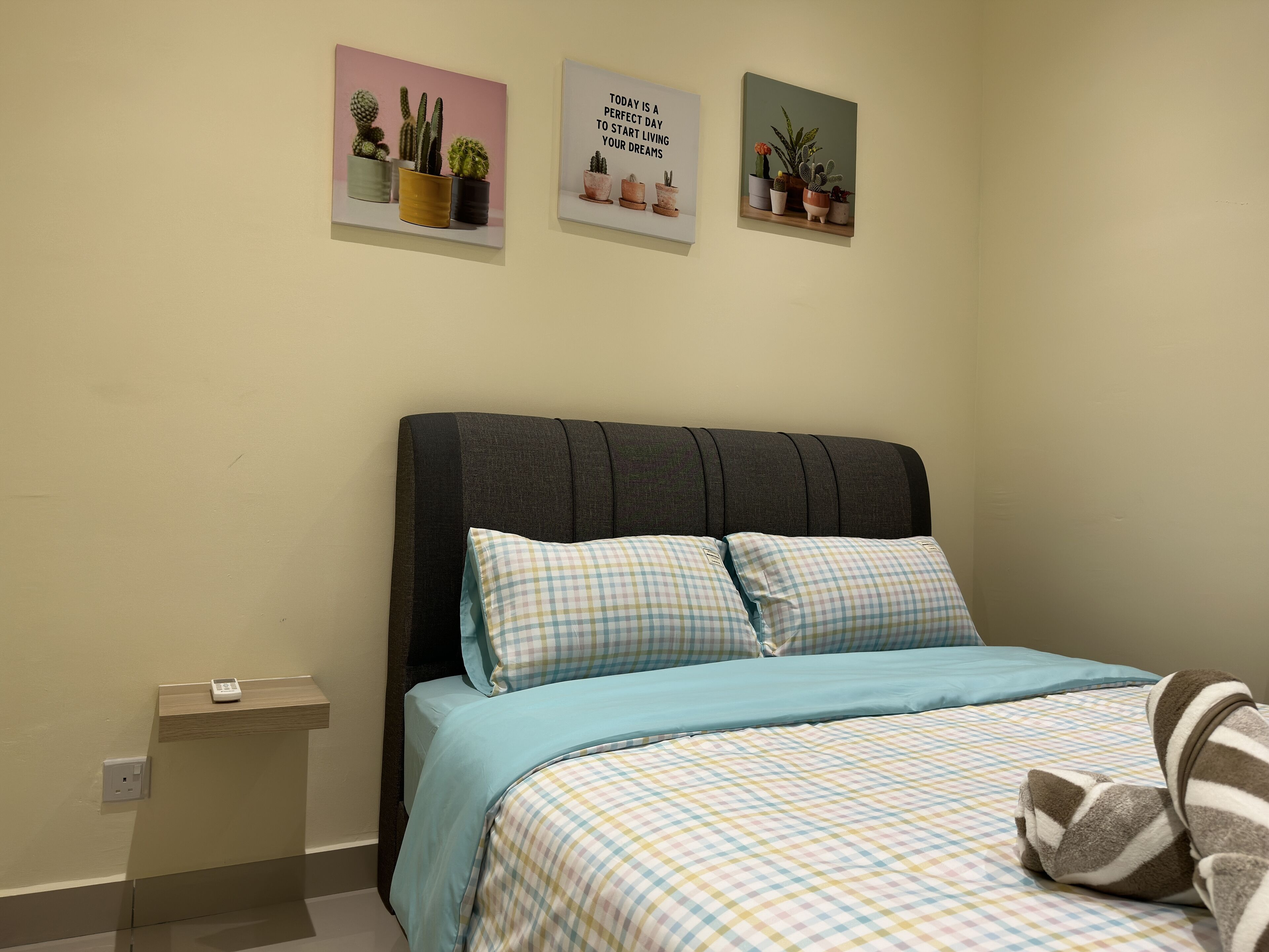 Un dormitorio con cama, almohadas, una mesita de noche y tres cuadros enmarcados en la pared.