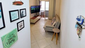 A living room with a sofa, TV, and wall decorations. - Complete apartment in Ubatuba - Itaguá with air conditioning + Wifi (Itaguá Ubatuba)