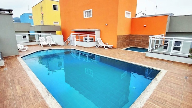 A rooftop swimming pool with a clear blue water surface, surrounded by white lounge chairs and a small sun terrace with a glass balustrade. - Complete apartment in Ubatuba - Itaguá with air conditioning + Wifi (Itaguá Ubatuba)