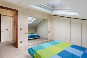 A bedroom with a skylight, a bed with a colorful bedspread, a wardrobe, and a mirror.