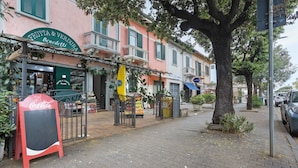 A street with a fruit and vegetable shop, a Coca-Cola sign, and a tree-lined sidewalk.