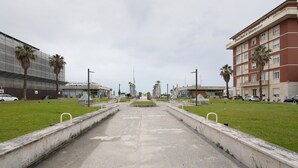 A pathway leading to a hotel with a modern building, palm trees, and a clear sky.