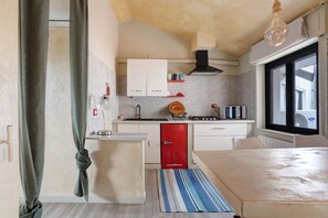 A compact kitchen with white cabinets, a red refrigerator, a gas stove, and a window with a view.