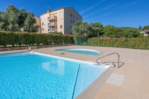 Une piscine avec une terrasse carrelée, un escalier en métal et un bâtiment doté de balcons en arrière-plan.