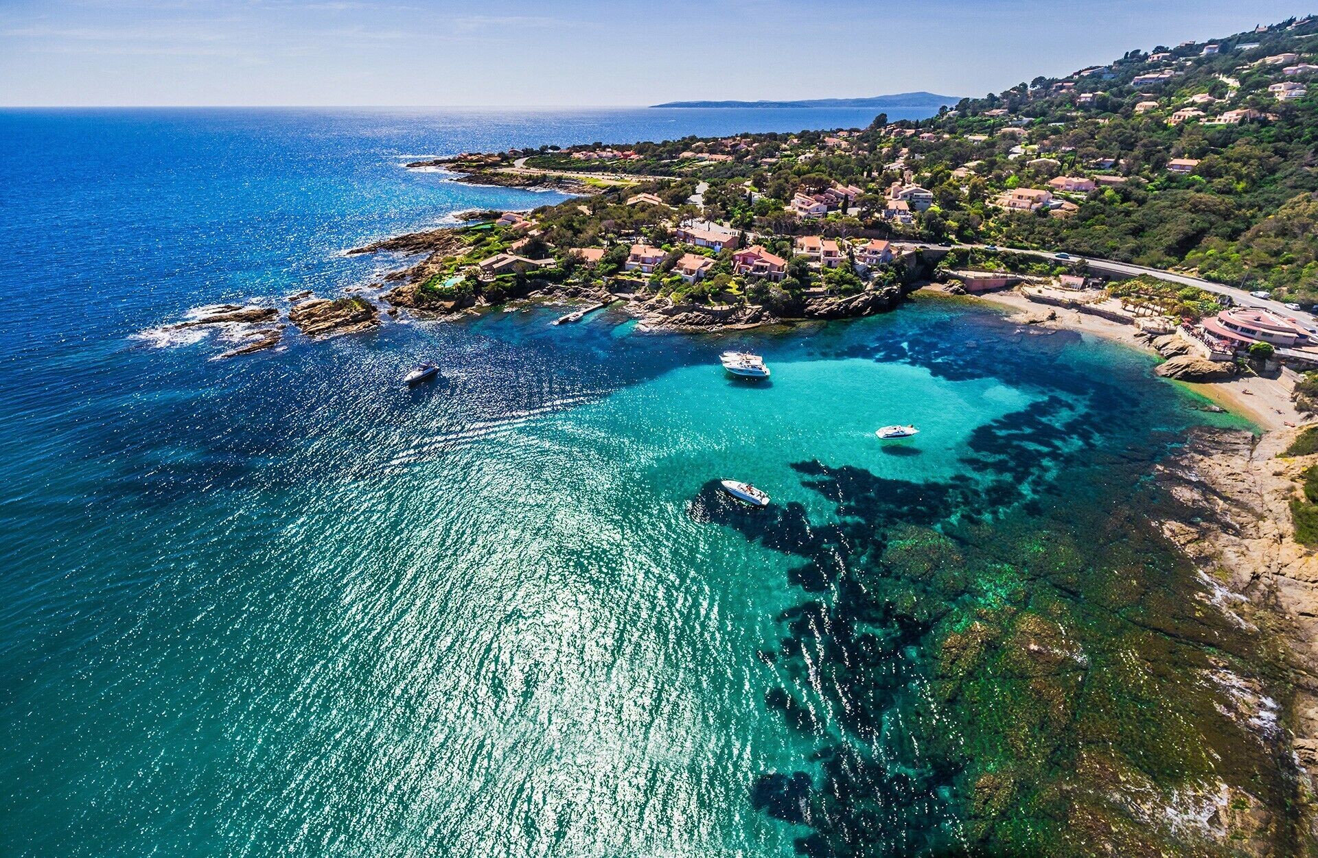 A coastal area with clear turquoise waters, boats, and a hillside settlement.