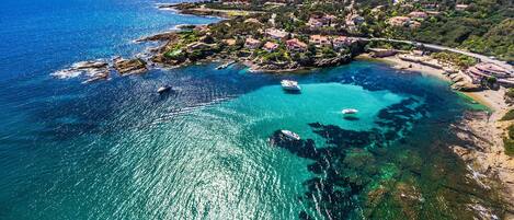 A coastal area with clear turquoise waters, boats, and a hillside settlement.