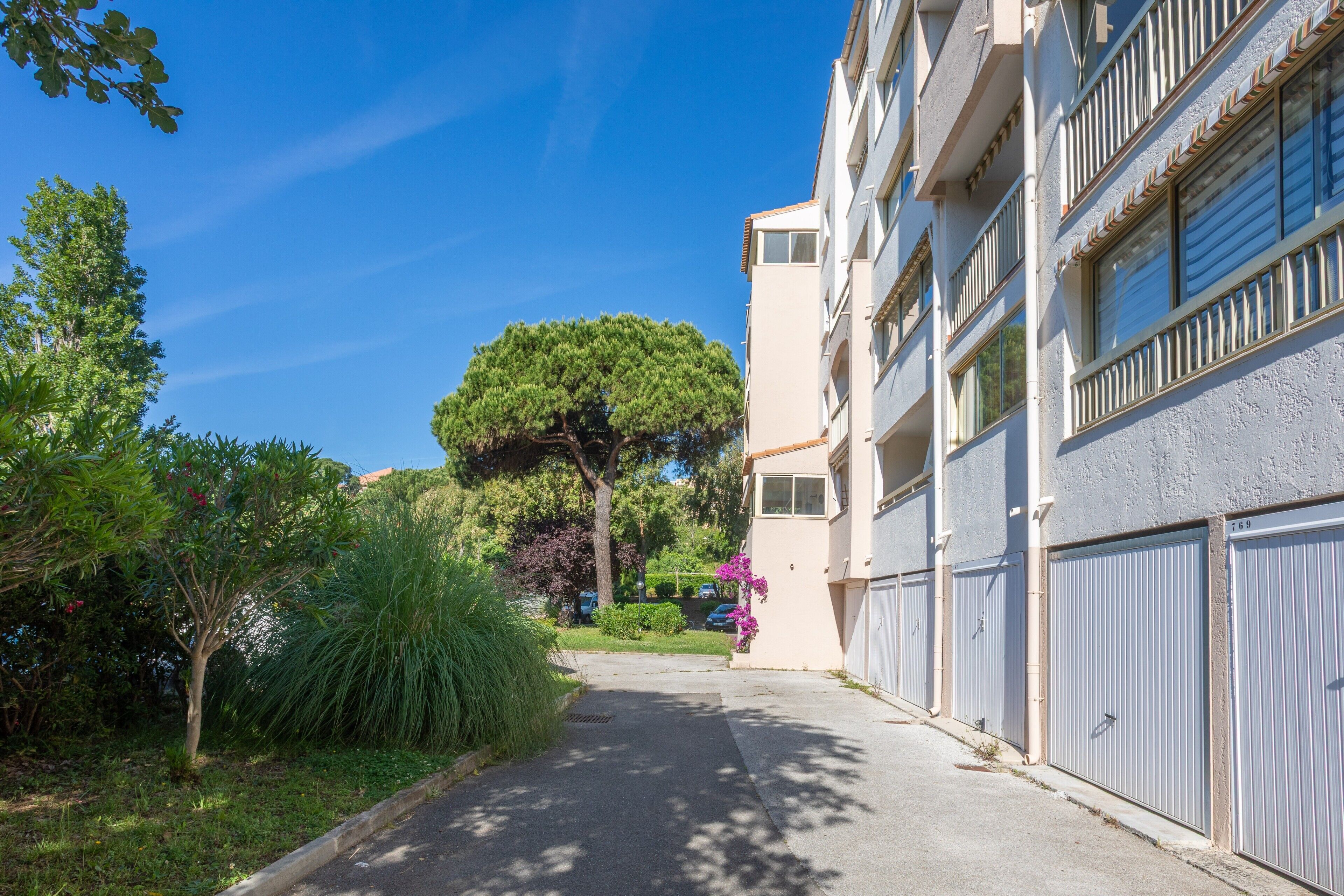A residential building with a garage door, a tree in front, and a clear blue sky.