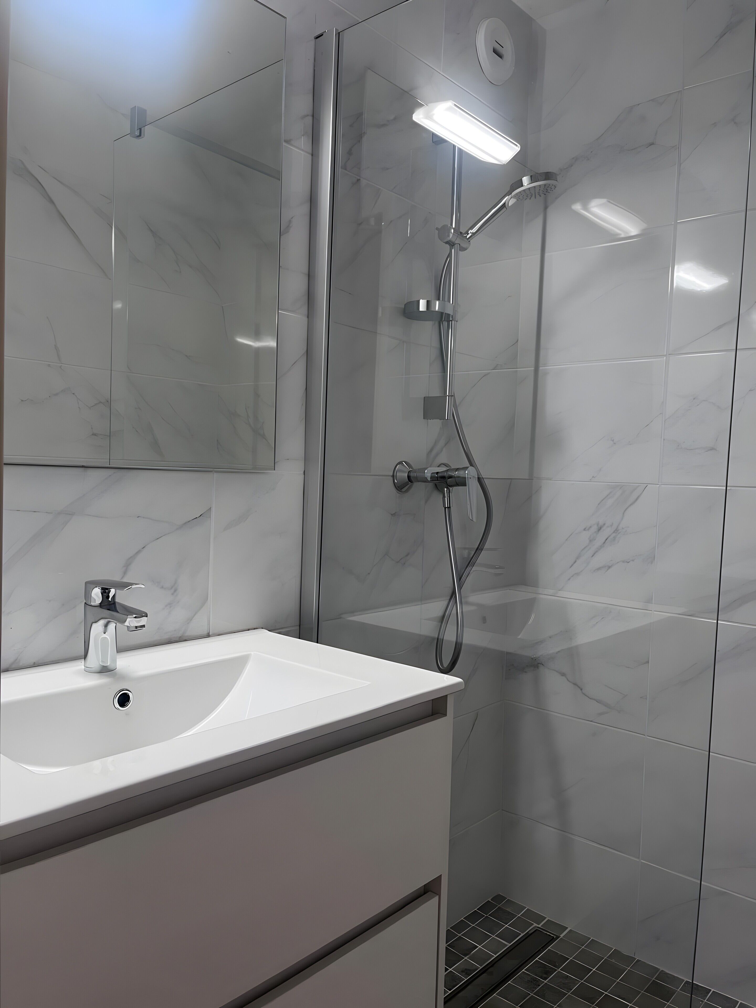 Un baño moderno con lavamanos de mármol blanco, cabina de ducha de vidrio y un espejo.