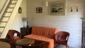 A living room with a sofa, two wicker chairs, a small table, a painting on the wall, a lamp, and a staircase. - Charming gîte in the Loire castles (Candes-Saint-Martin)