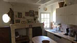 A kitchen with a fireplace, wooden table, and white cabinets. - Charming gîte in the Loire castles (Candes-Saint-Martin)