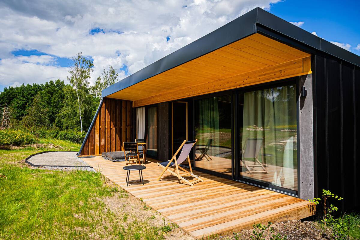 A modern house with a wooden deck, large glass windows, and outdoor seating.