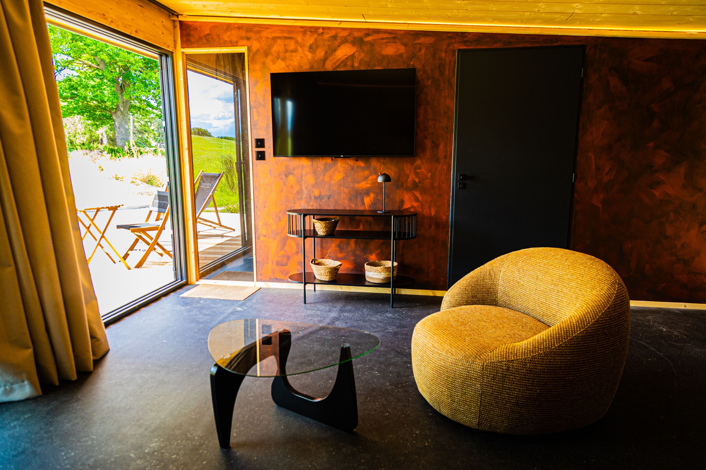 Un salón moderno con un televisor grande, un sillón redondo tejido y una mesa de centro de vidrio.