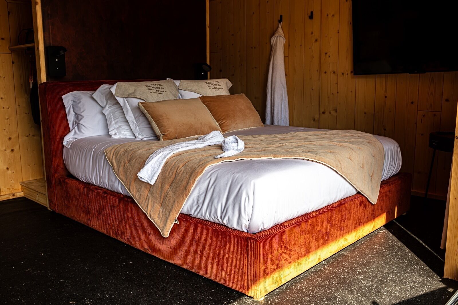 Uma cama com estrutura vermelha, roupa de cama branca e manta bege.